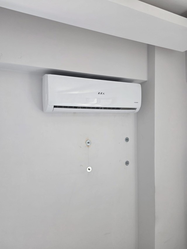Boş bir odada duvara asılı iç ünite; panel kapalı ve gövde temiz