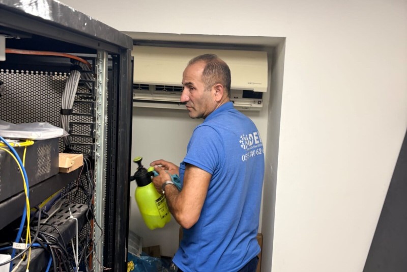 Tekniker acik sunucu kabini onunde sprey sisesiyle calisiyor; arkada duvar tipi ic unite