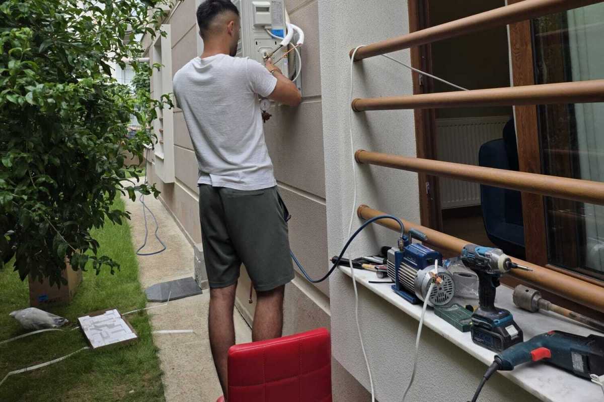 Tekniker dış ünitede manifold manometreyle çalışıyor, pencere kenarında vakum pompası ve el aletleri